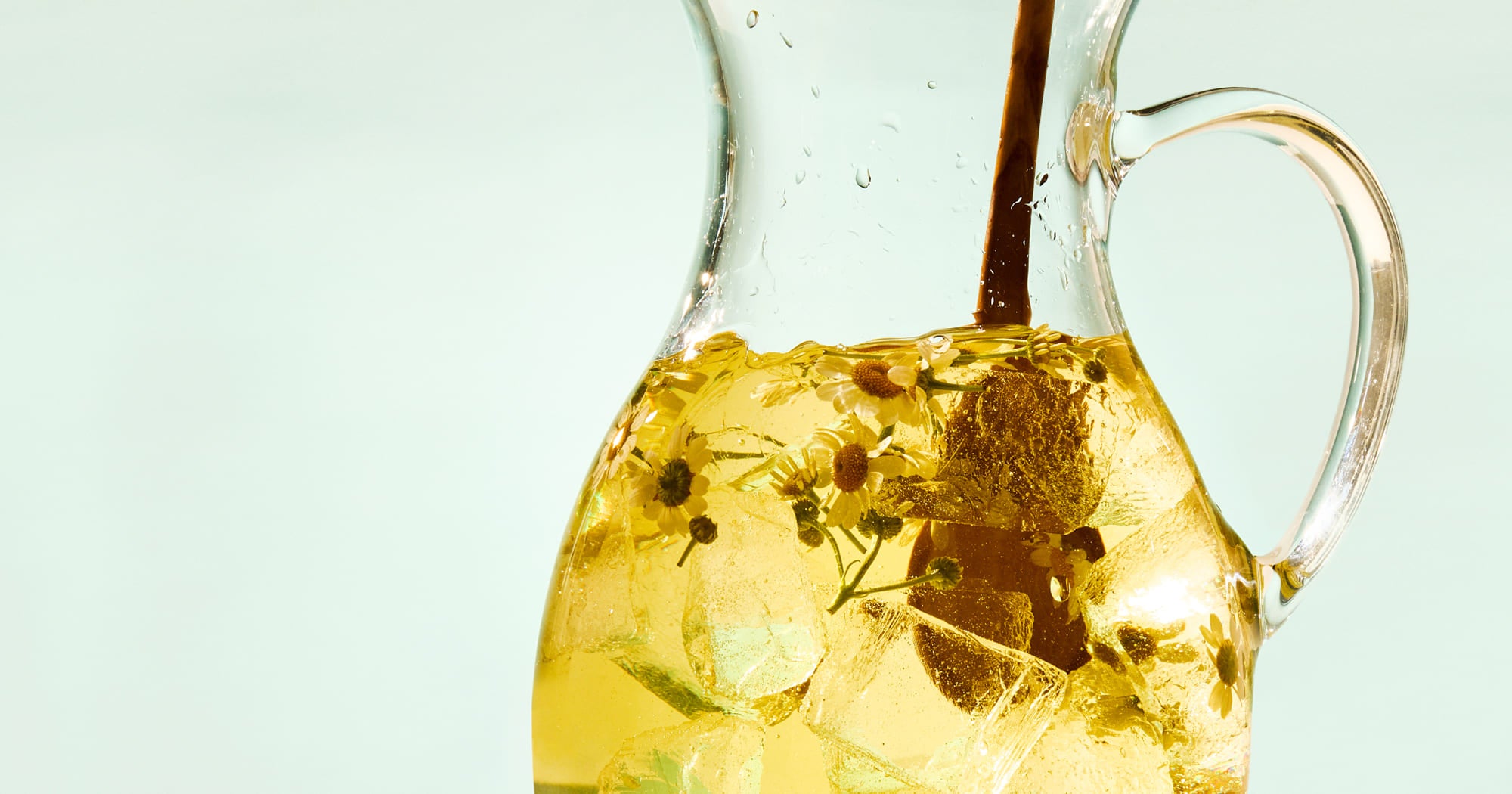 Clear glass pitcher filled with iced tea on a light blue background
