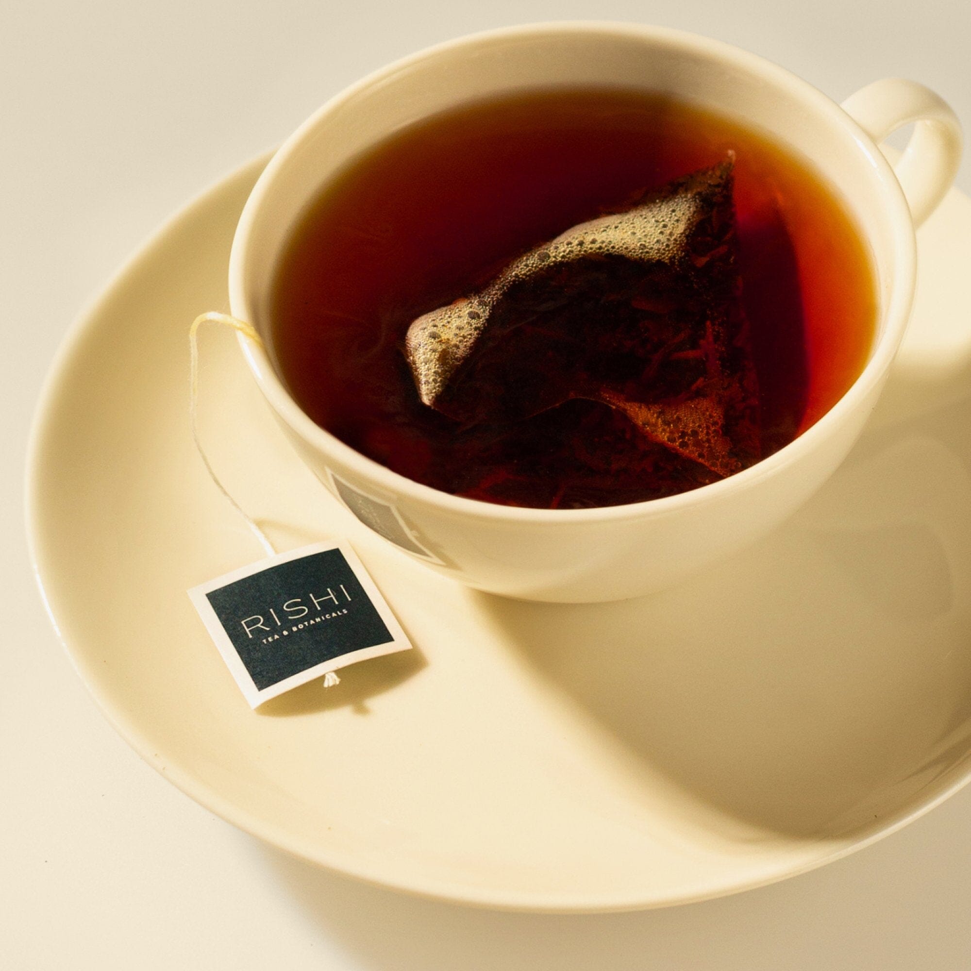 A white cup of tea with a tea bag steeps on a matching saucer. The label reads