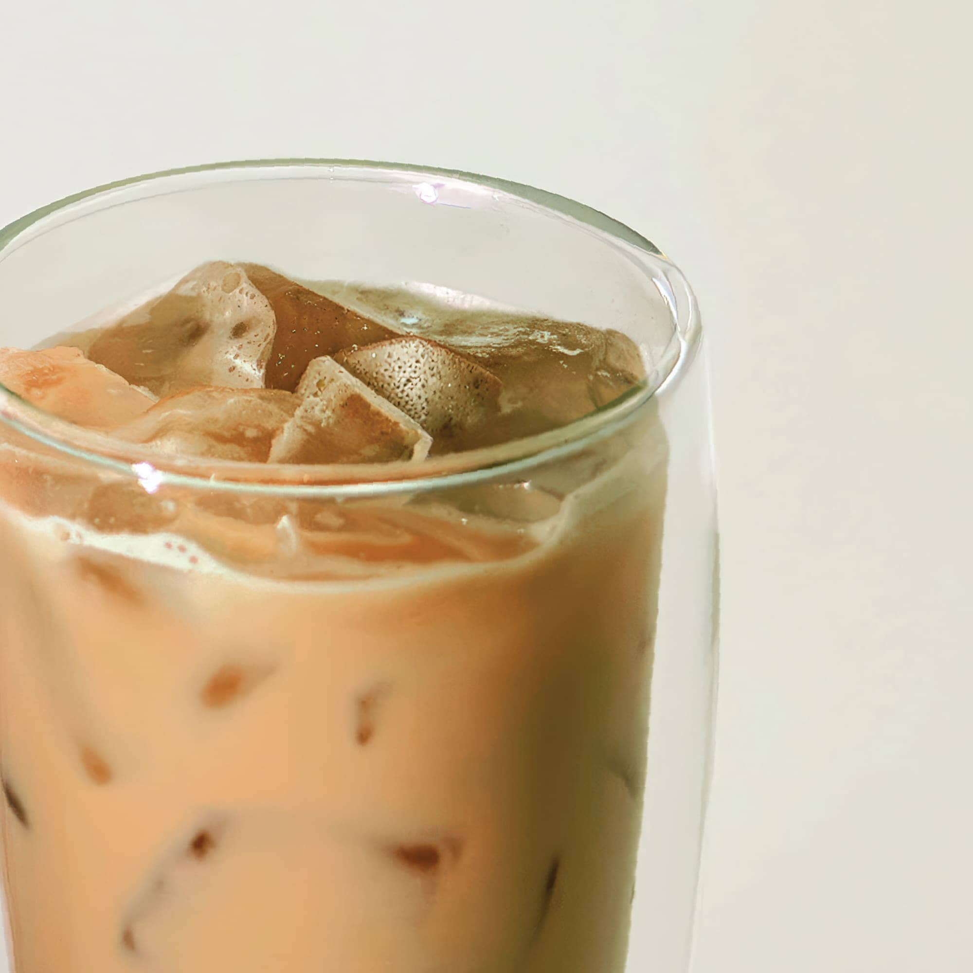 A close-up of a glass filled with Rishi Tea & Botanicals iced Houjicha tea, showcasing ice cubes and a light brown brew with roasted malty notes against a plain background.