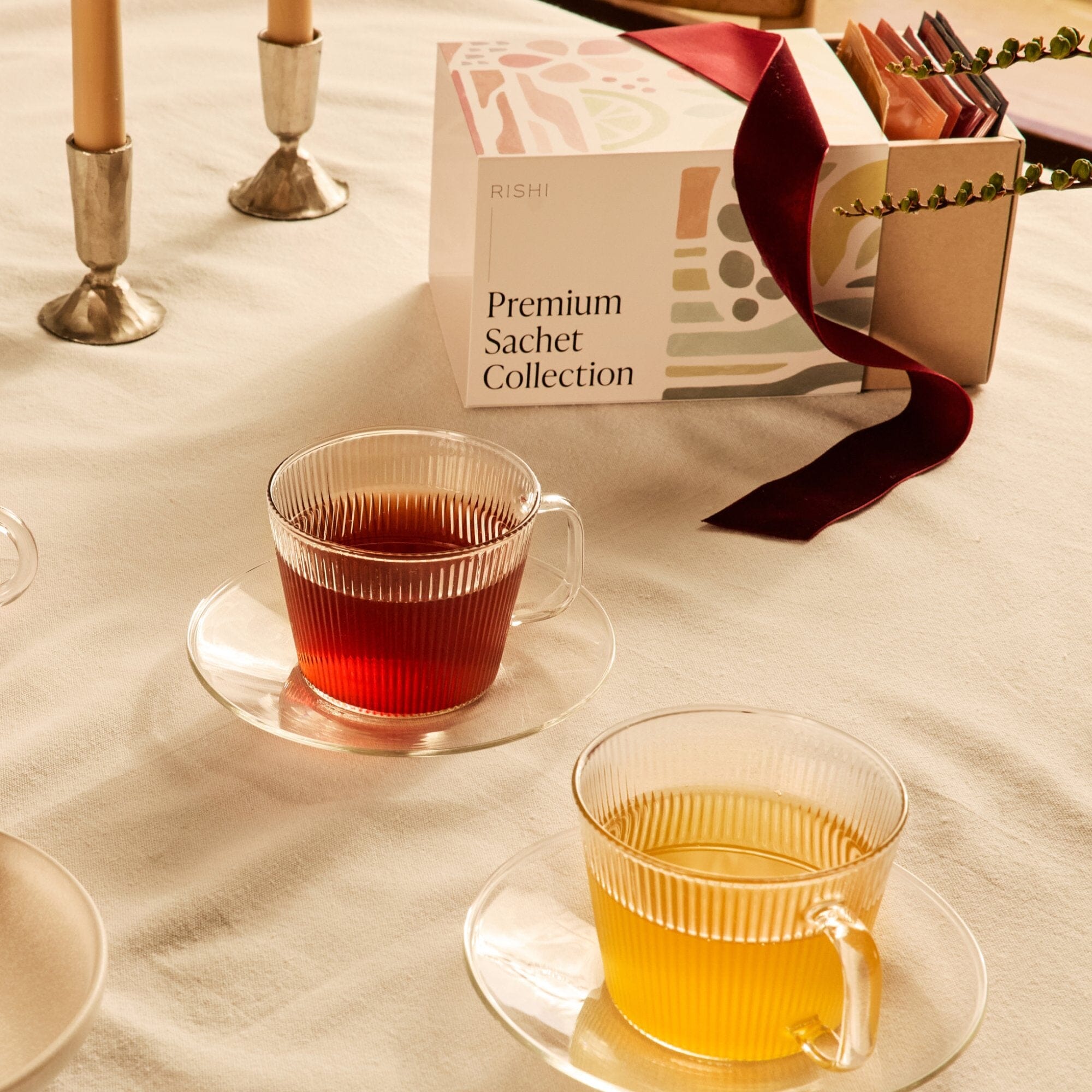 Two clear glass teacups with red and yellow tea from Rishi Tea & Botanicals sit on saucers beside a box labeled