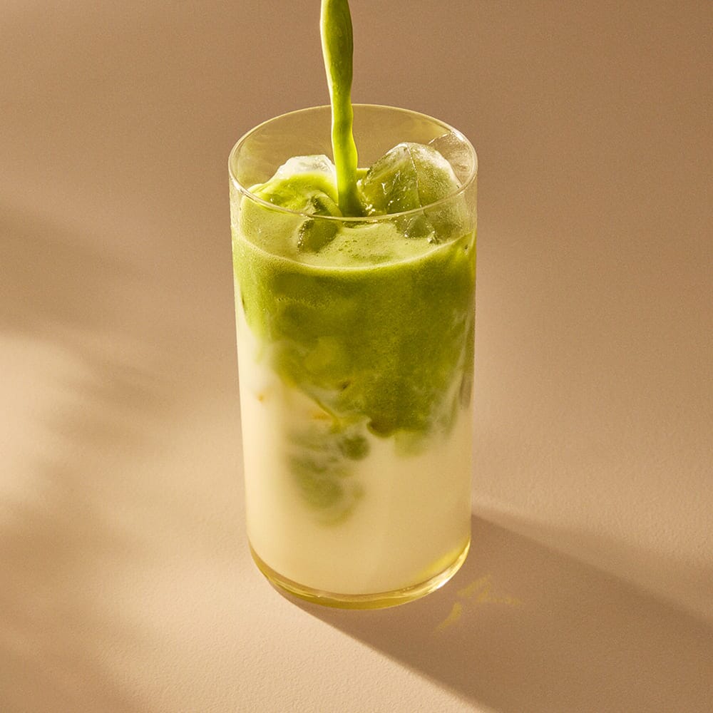 Organic matcha from Rishi Tea & Botanicals is poured into iced milk, forming swirling patterns on a light-colored surface.