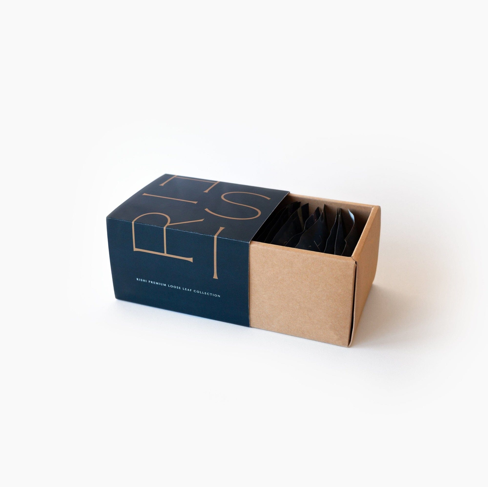A partially opened Rishi Tea & Botanicals box features dark navy and gold lettering, offering a luxurious tea experience. Inside, black packets are visible, showcasing a minimal and modern design on a white background that invites you to explore the rich flavors of organic loose leaf teas.