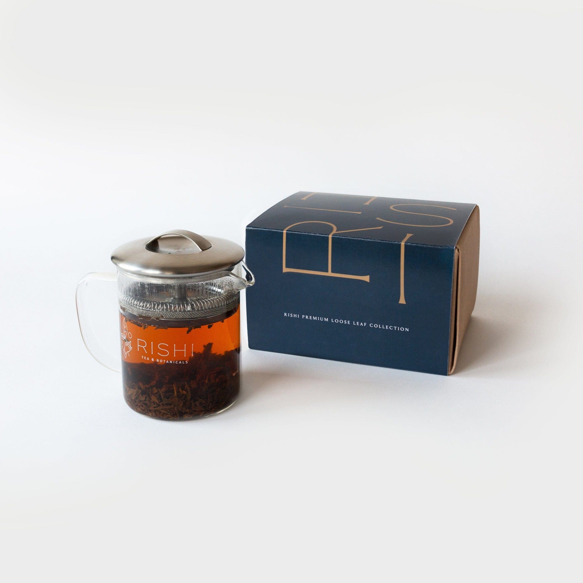 A glass teapot with brewed tea rests next to a dark blue box marked