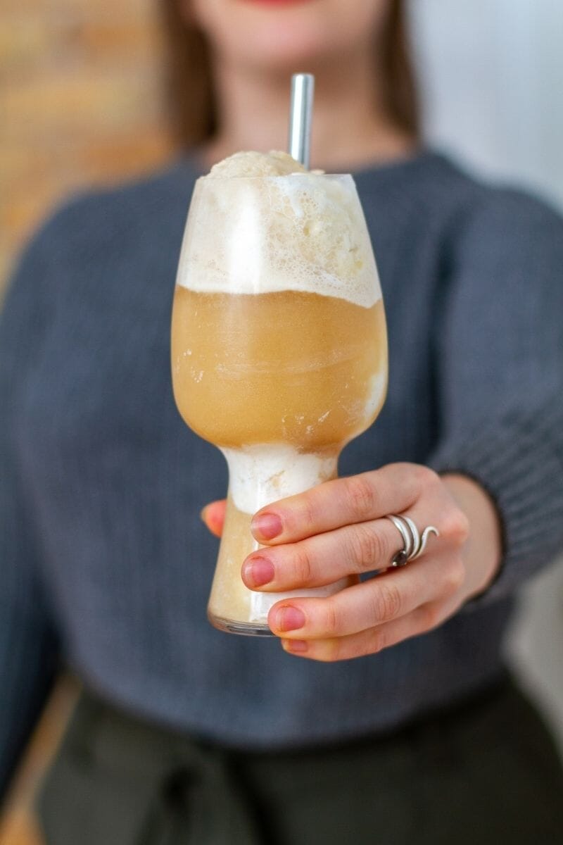 a person holding a dandelion ginger Italian soda in a tulip glass with a straw towards the camera