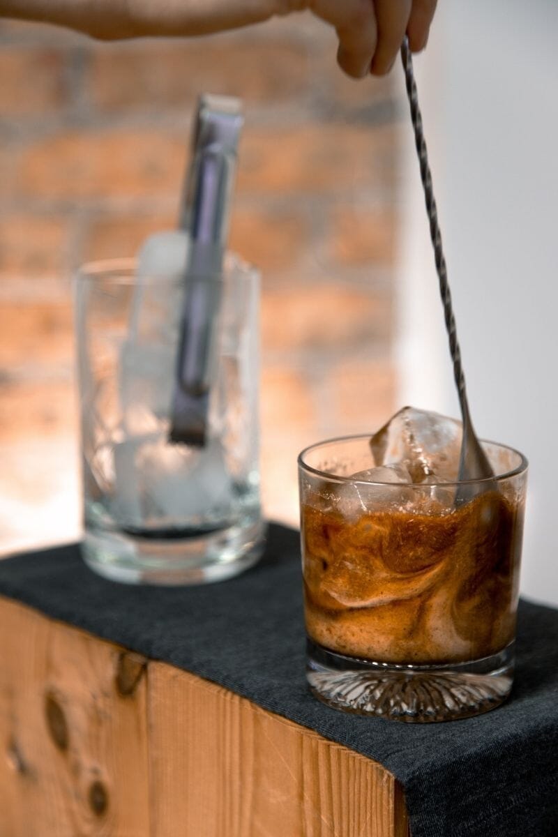 Bartender stirring a mushroom white russian with ice in a rocks glass. The cream is swirling with the mushroom liqueur.