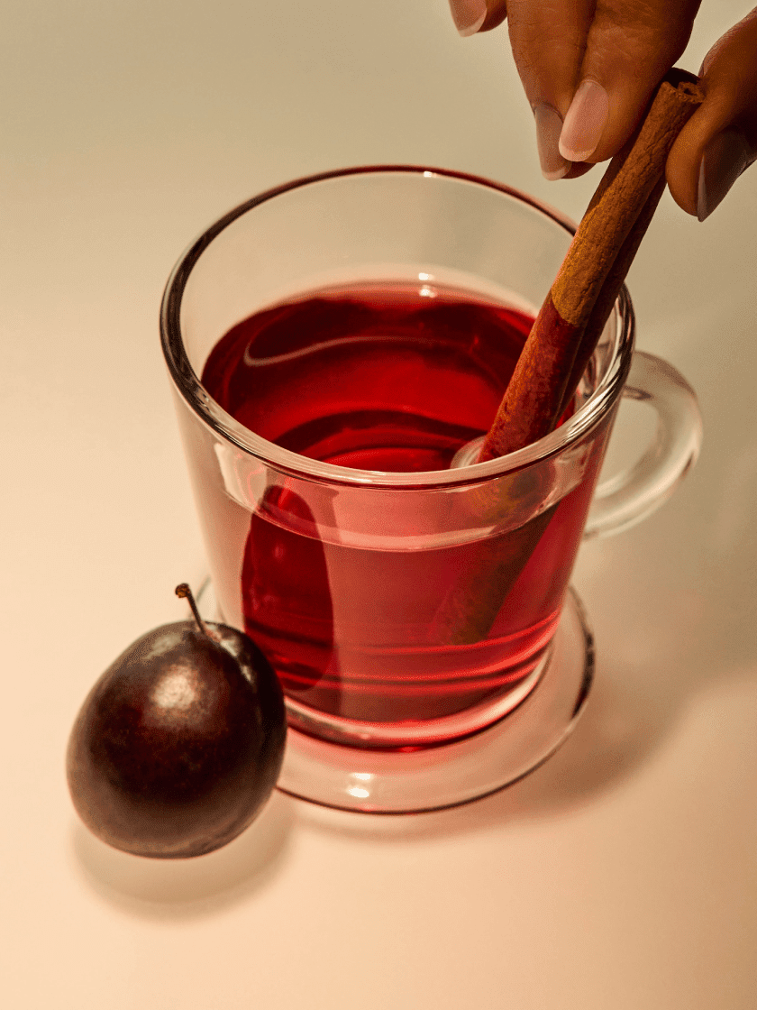 A white teapot with a tea bag label beside two filled teacups on saucers. A brass tray and red-purple leaves are visible on a white tablecloth.