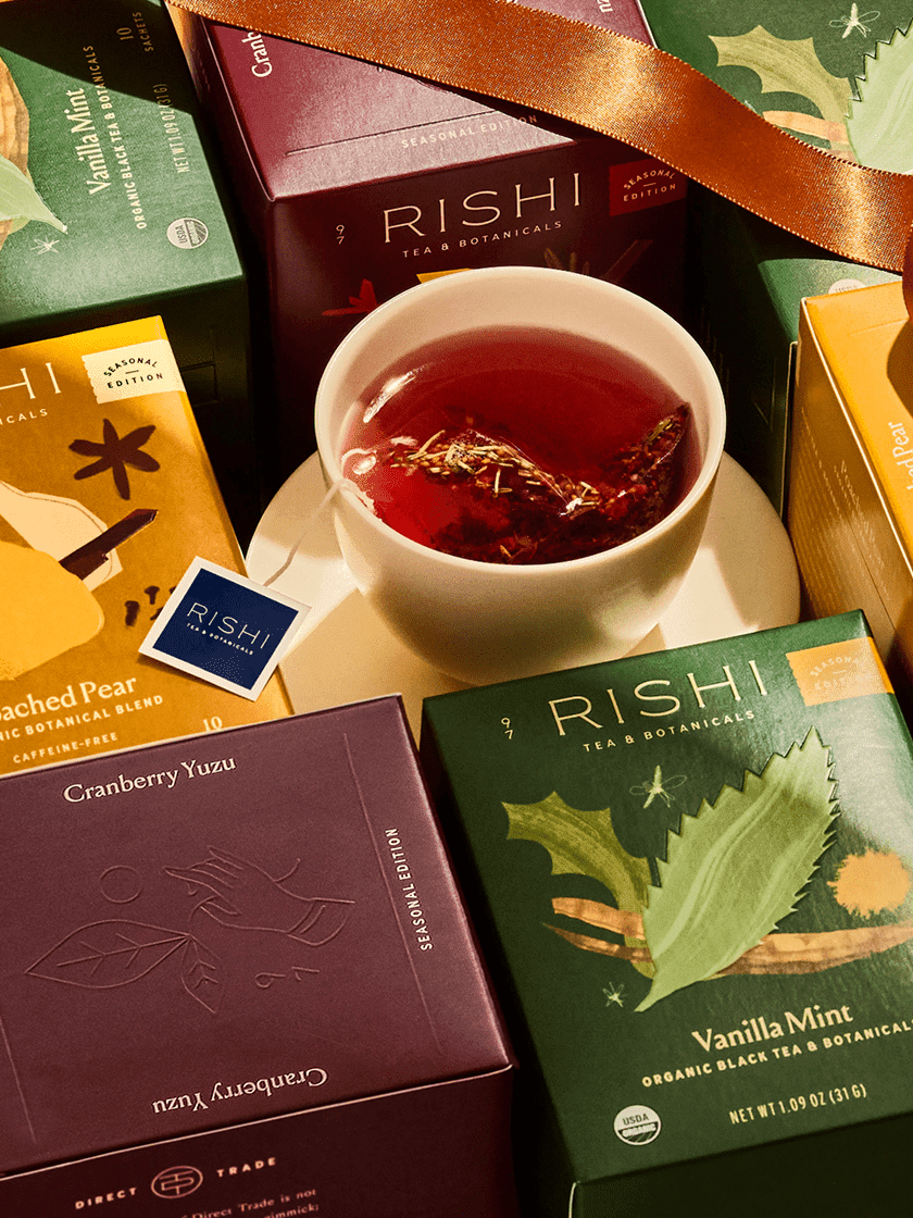Tea bags in a colorful box with two cups of tea and an orange segment on a table.