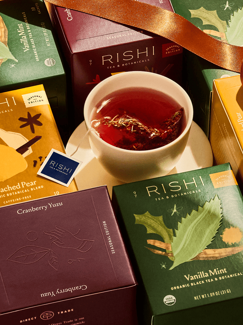 Tea bags in a colorful box with two cups of tea and an orange segment on a table.