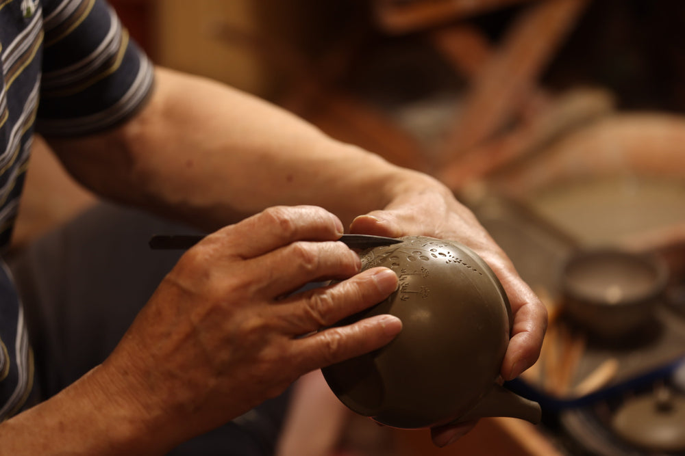 Person shaping a clay pot on a pottery wheel in a workshop.