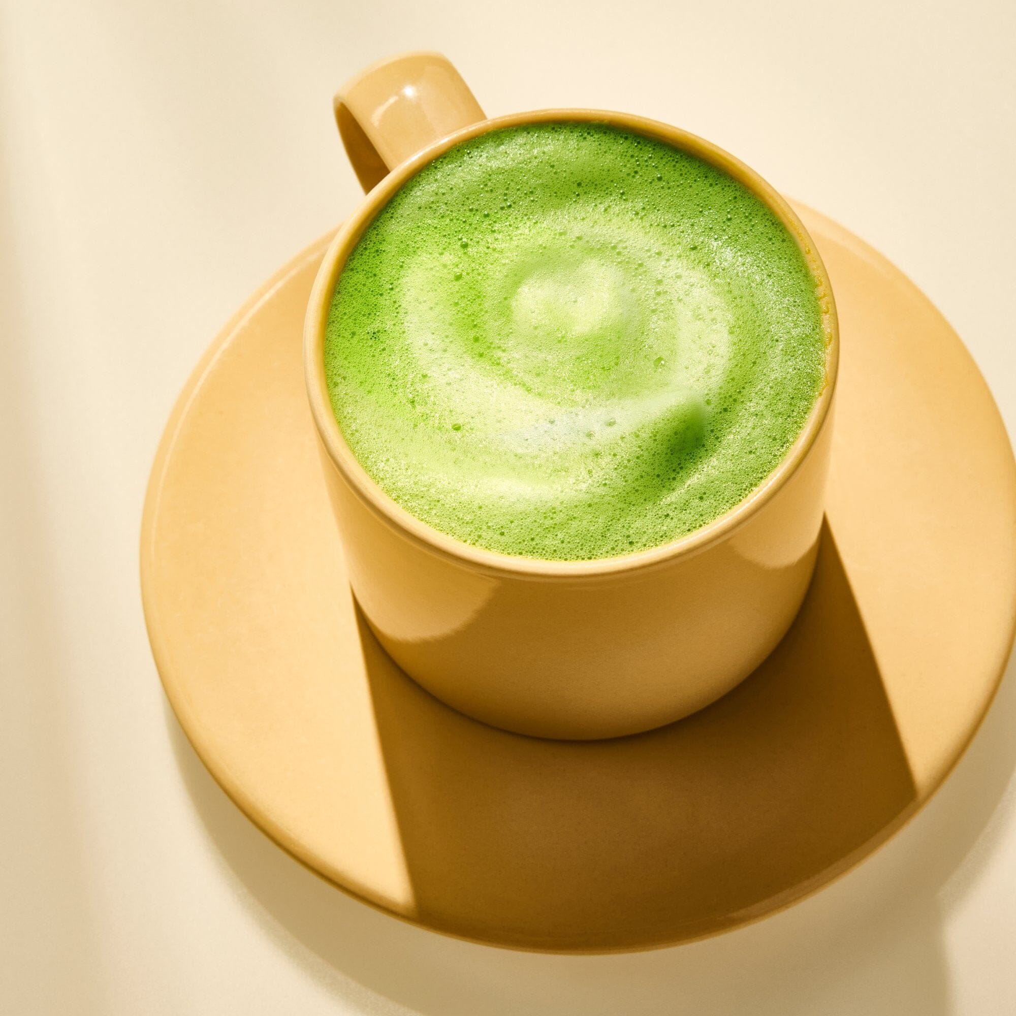 A beige cup and saucer holds a frothy Barista Matcha latte from Rishi Tea & Botanicals, topped with a swirl pattern and photographed in bright, even light.