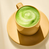 A beige cup and saucer holds a frothy Barista Matcha latte from Rishi Tea & Botanicals, topped with a swirl pattern and photographed in bright, even light.