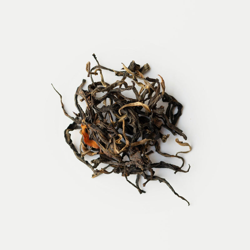 Loose, dried Snow Shan red tea leaves by Rishi Tea & Botanicals from Vietnam, showing orange and brown hues, are arranged on a simple white background.