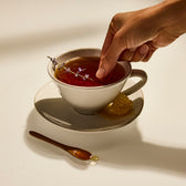 Hand placing a sprig of lavender into a cup of tea with a spoon on a saucer