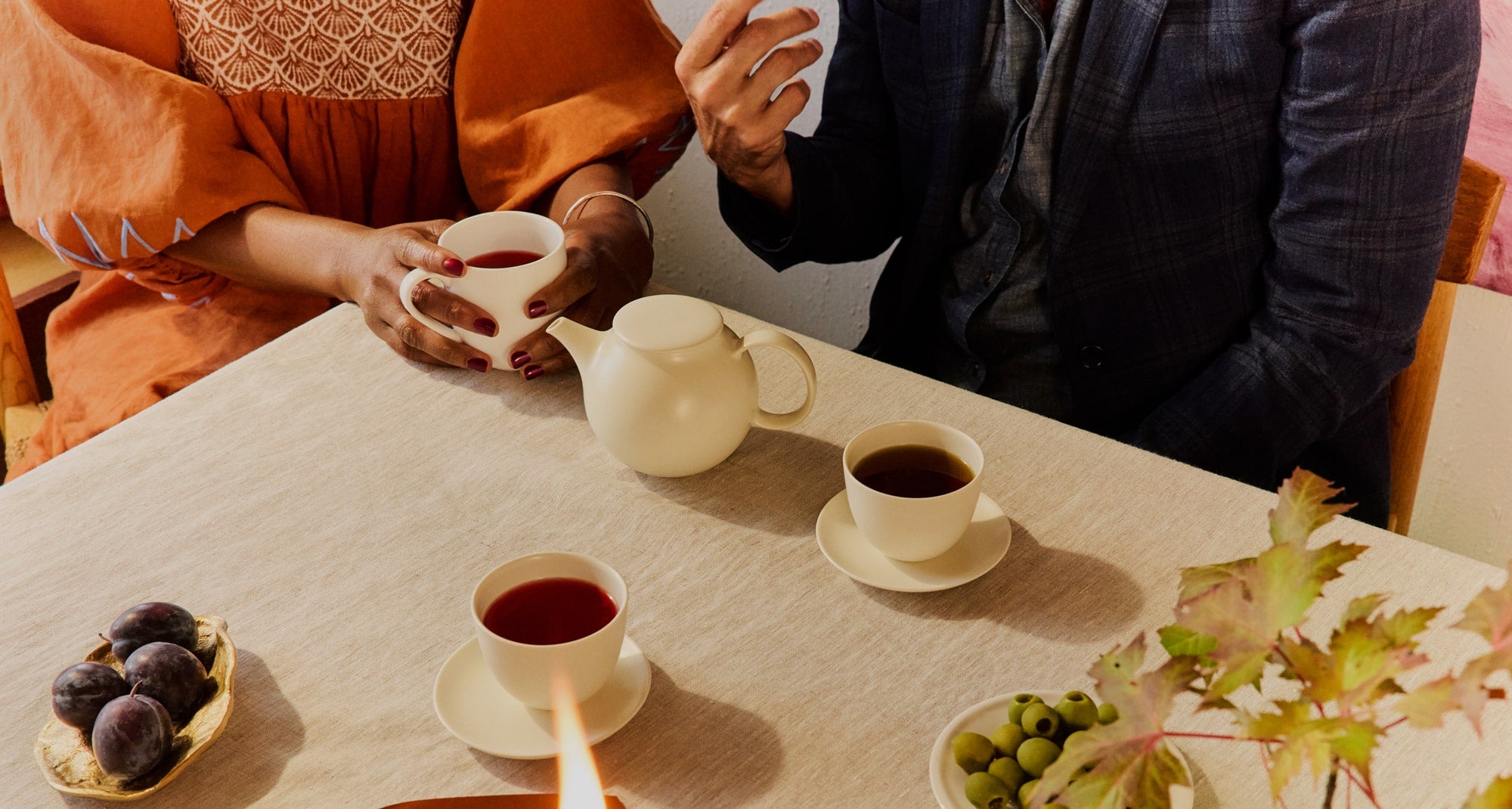 Two people sitting at a table with tea cups and snacks, one person is pouring tea.