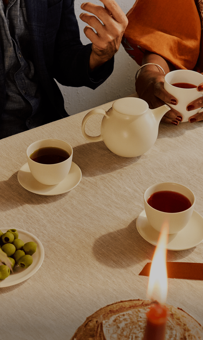 Two people sitting at a table with tea cups and snacks, one person is pouring tea.