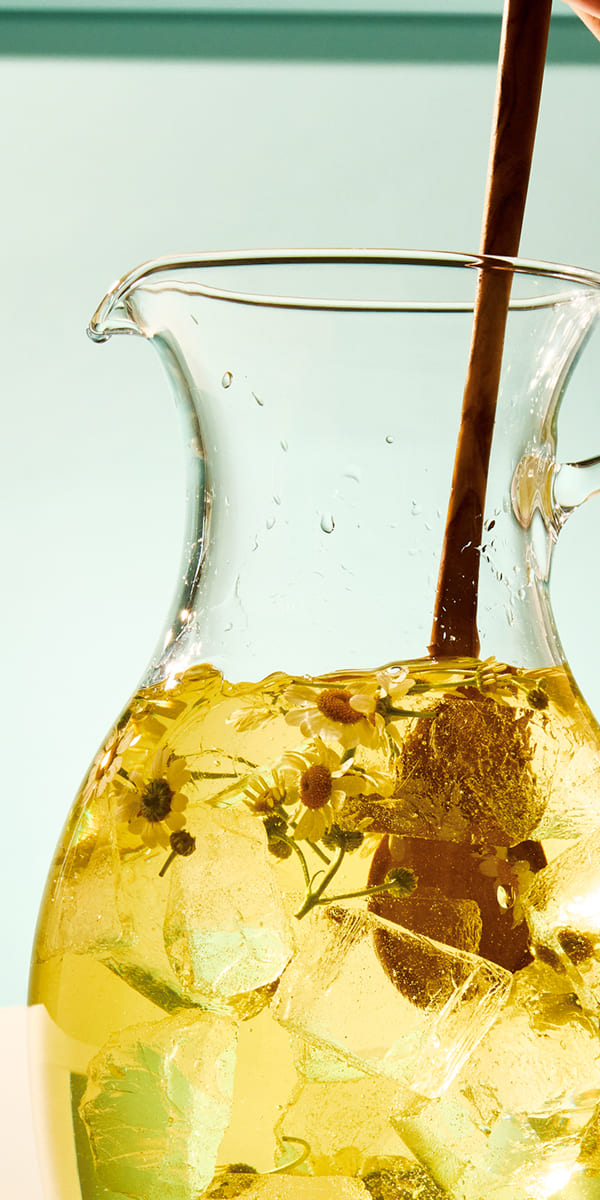 Glass pitcher filled with a yellow liquid and ice cubes on a light background