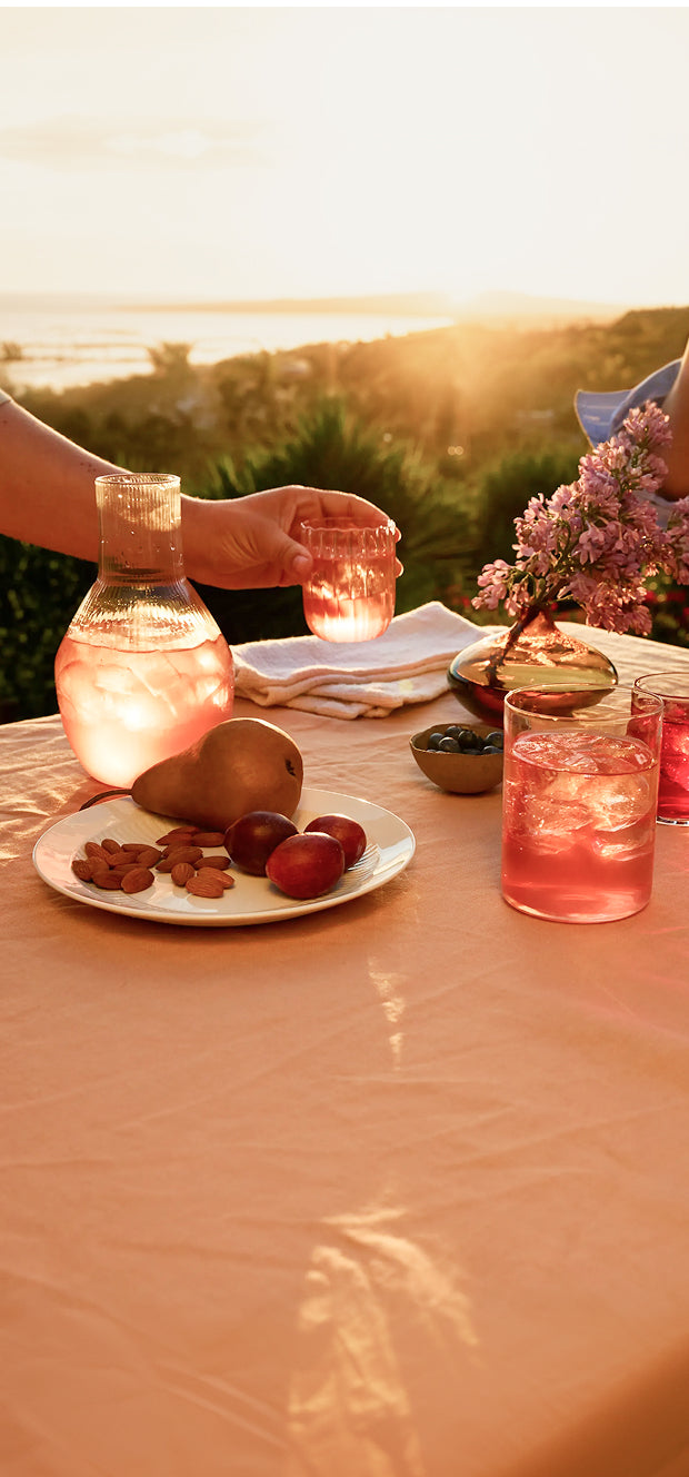 Sunset tablescape of two people's hands interacting with a pitcher and glasses of iced tea with a natural background