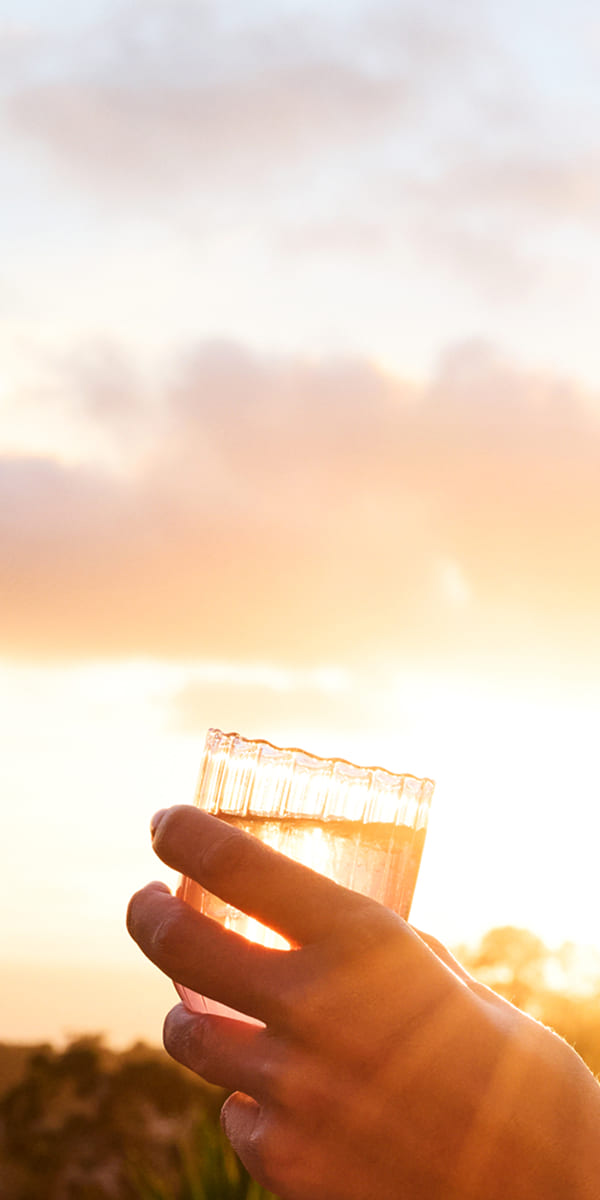 Hand holding a glass of tea with a sunset in the background