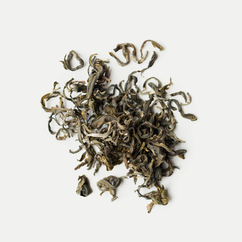 Loose, dried Vietnam tea leaves are scattered on a plain white background.