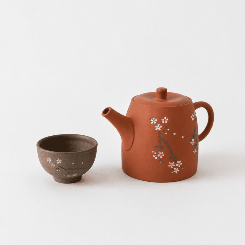 A brown Tokoname teapot by Chato Co., Ltd. with a cherry blossom motif sits beside a matching teacup on a white background.
