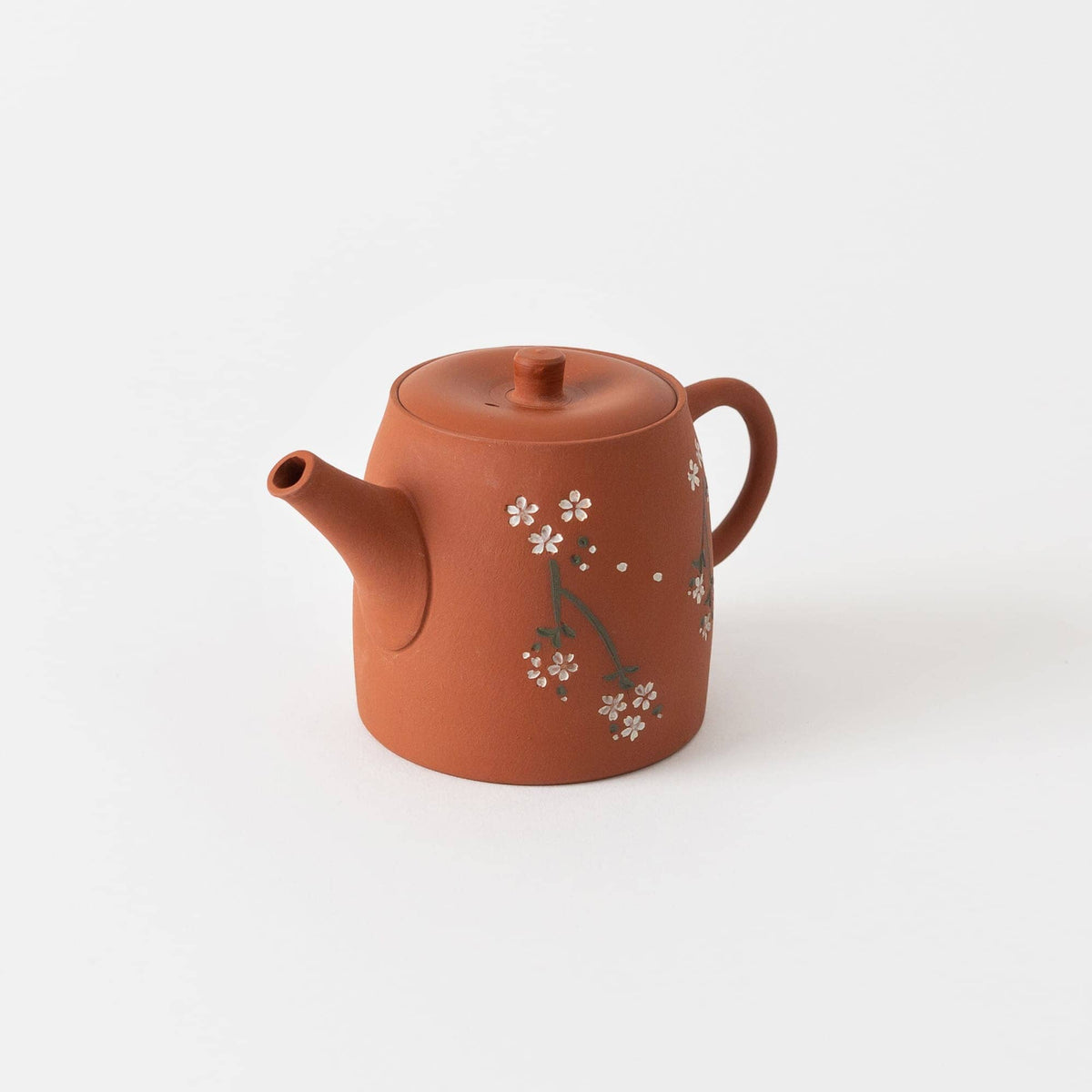 A brown ceramic teapot with lid by Chato Co., Ltd., crafted from shudei clay by a Tokoname potter, featuring a simple floral design of white flowers and green stems, displayed on a plain white background.