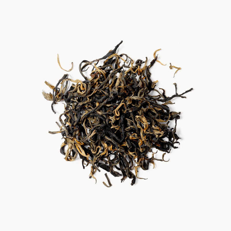 Loose leaf Assam tea from Rishi Tea & Botanicals, featuring forest-grown twisted dark and golden leaves, displayed in a small pile on a white background.