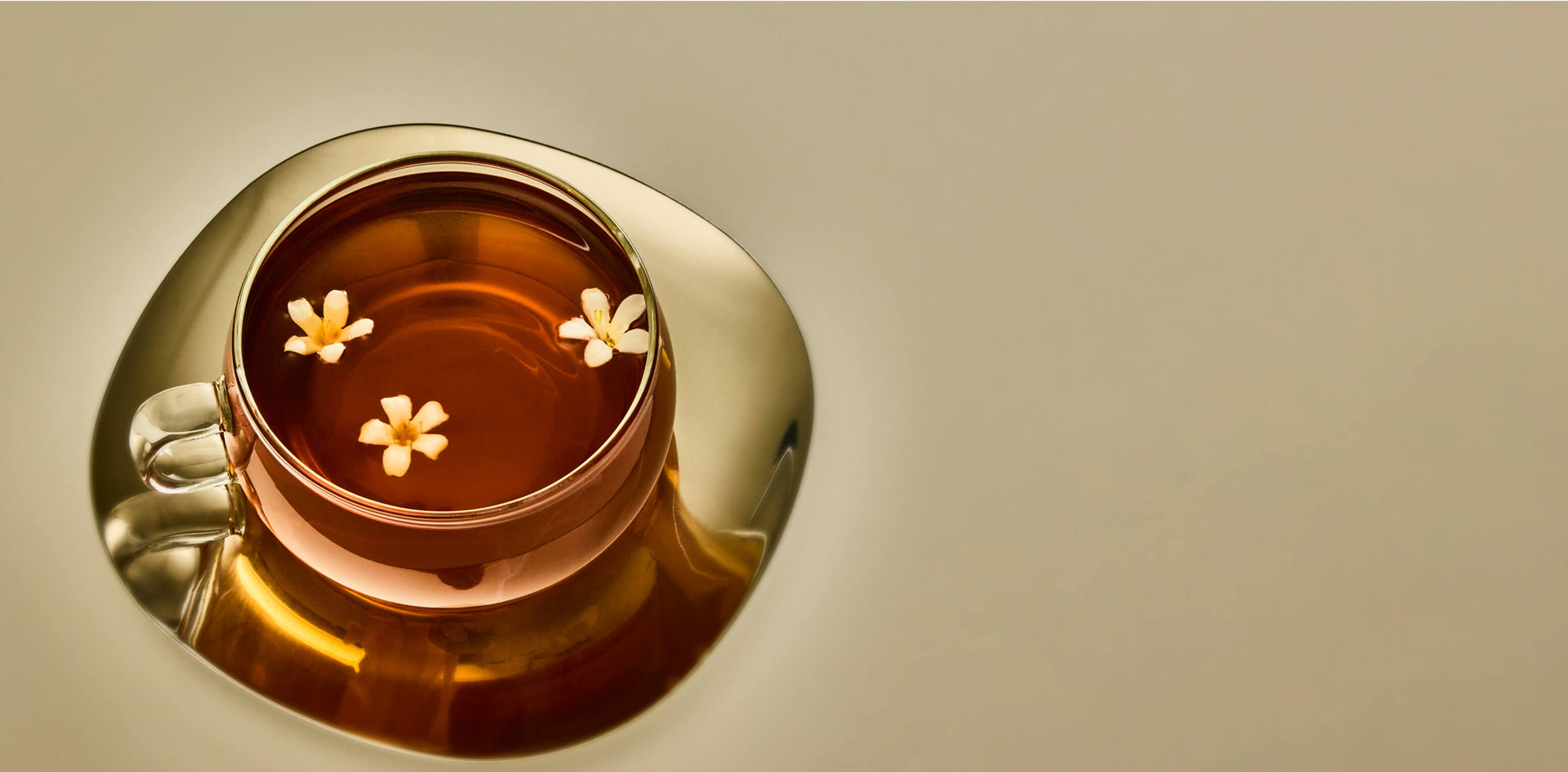Gold cup and saucer with tea and flowers on a beige background
