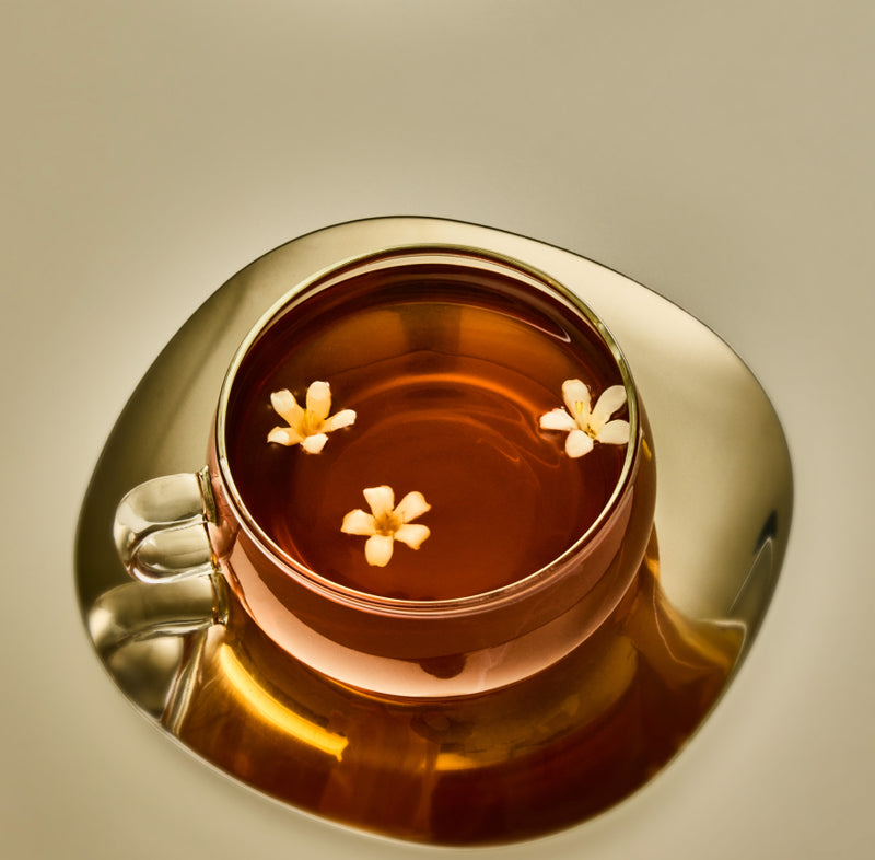 Gold cup and saucer with tea and flowers on a beige background