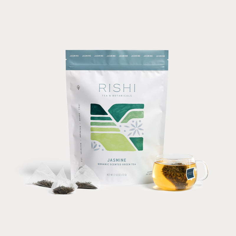 A bag of Rishi Tea & Botanicals Jasmine Green high mountain tea is displayed with three pyramid tea bags, loose leaves, and a clear glass cup of fragrant brewed tea.