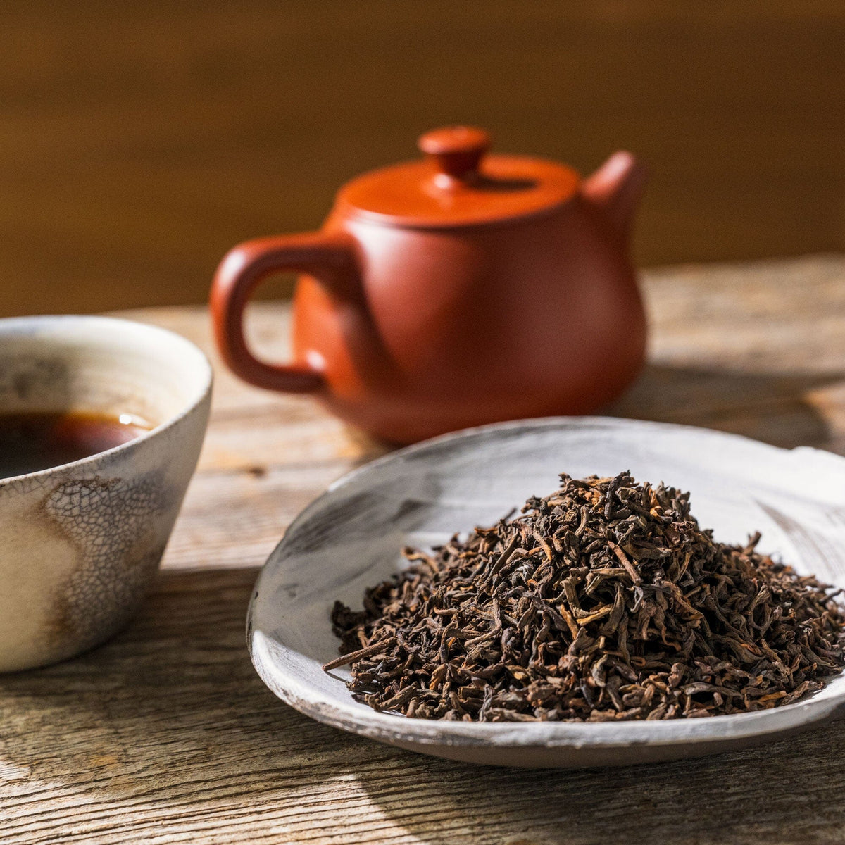 A bowl of Pu’er Classic tea and a Rishi Tea & Botanicals teapot on a wooden table.