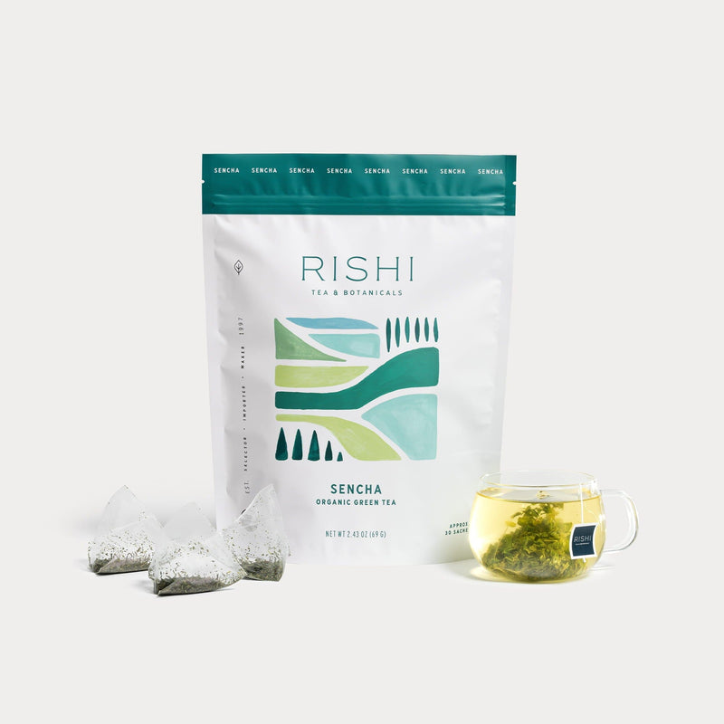 A bag of Rishi Tea & Botanicals Sencha organic green tea appears with pyramid tea bags and a clear glass cup of brewed green tea, highlighting soothing, aromatic notes for a calming experience.