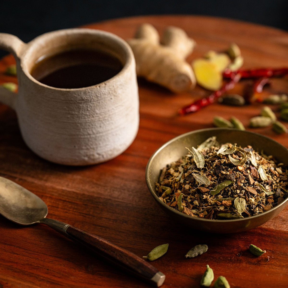 A cup of Spicy Masala Chai and a bowl of spices on a wooden table from Rishi Tea & Botanicals.