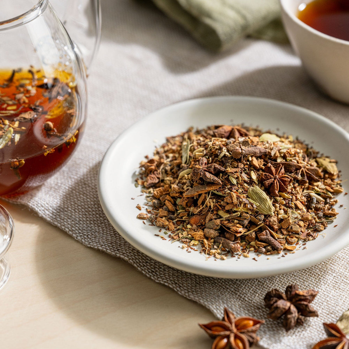 A cup of West Cape Chai by Rishi Tea & Botanicals with spices and herbs on a table.