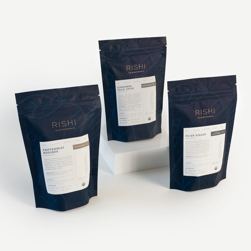 Three Rishi Tea & Botanicals wellness teas—Peppermint Rooibos, Cinnamon Tulsi Spice, and Pure Ginger—are displayed upright on a white surface, with one elevated to highlight this energizing tea bundle.