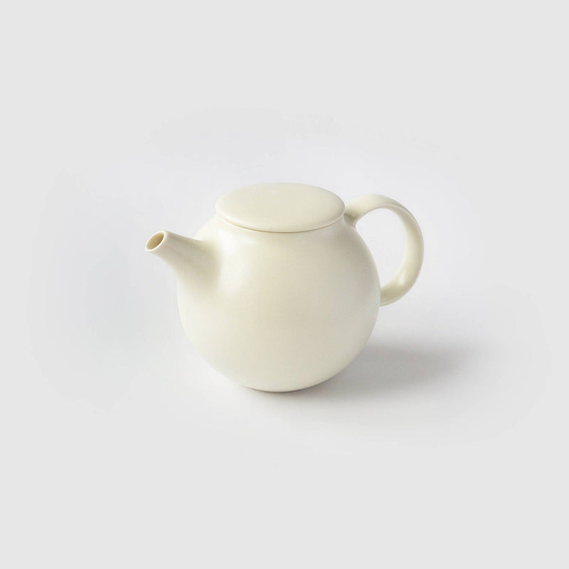 A Kinto USA, Inc plain white Pebble teapot with a short, drip-free spout and round handle elegantly rests on a white surface against a light gray background.