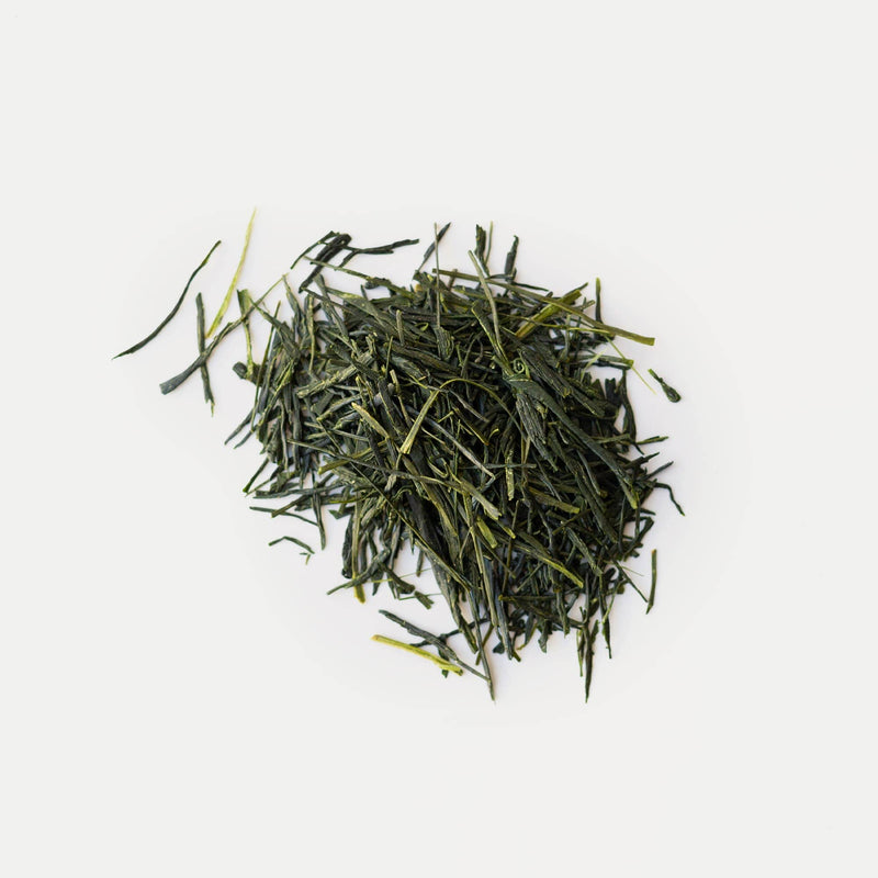 A pile of loose, dried green tea leaves, including Hon Yama Shincha Okouchi from Rishi Tea & Botanicals, displayed on a plain, light background.
