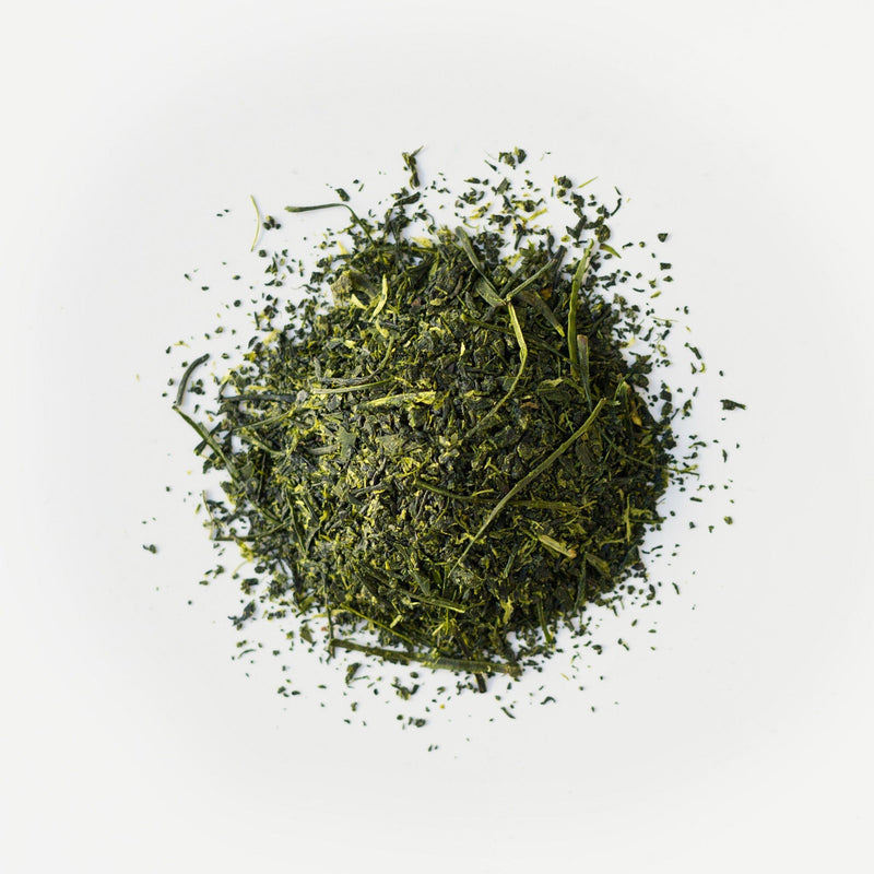 A pile of loose, dried sencha green tea leaves from Rishi Tea & Botanicals rests on a plain white background, their vibrant color reflecting the rich nutrients of volcanic soil near Mount Fuji.