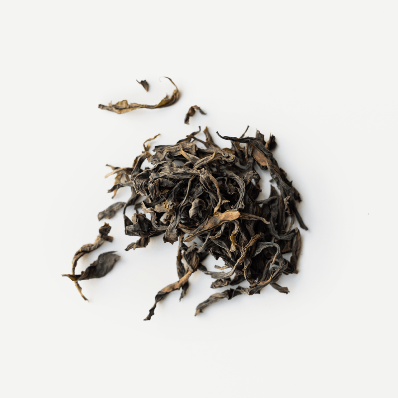 A pile of loose, medium-roasted Wuyi rock tea leaves, like Golden Peony oolong from Rishi Tea & Botanicals, rests on a white background.