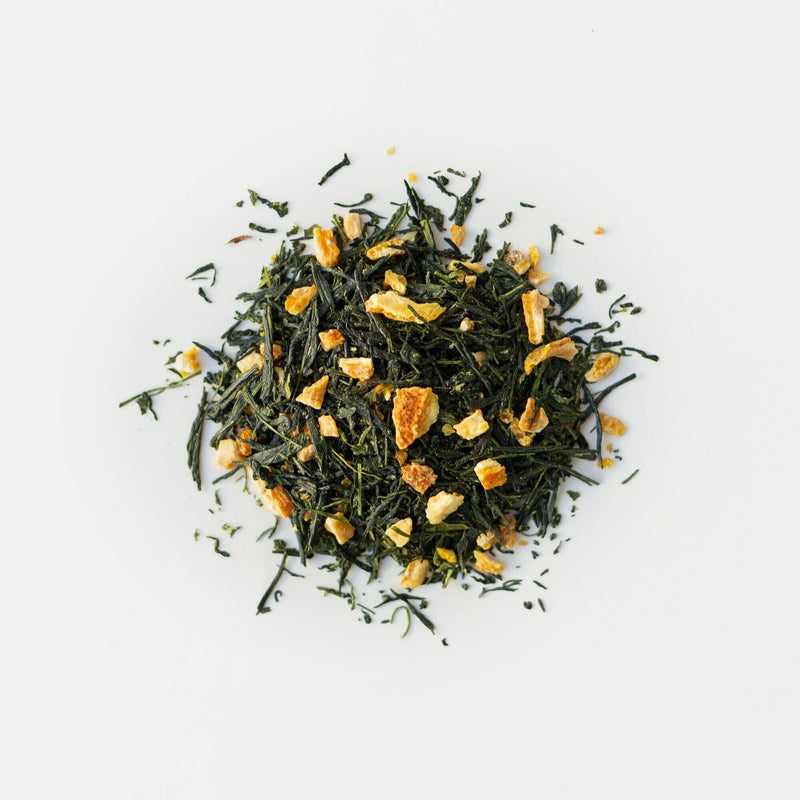 A pile of loose leaf sencha green tea mixed with small dried orange peel pieces from Rishi Tea & Botanicals on a white background, ideal for yuzu tea enthusiasts.