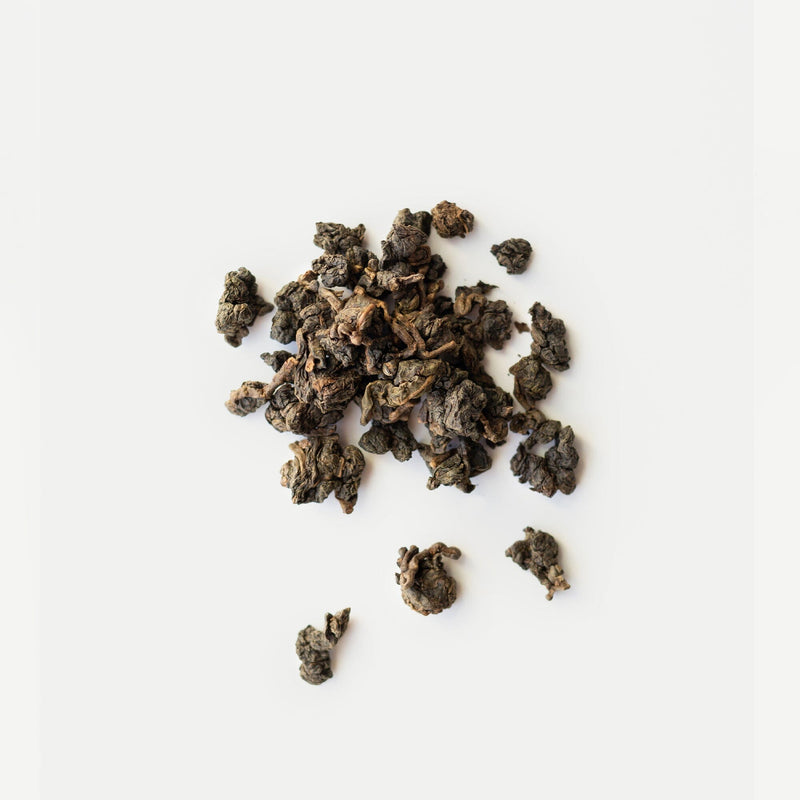 Rishi Tea & Botanicals’ hand-harvested, loose-rolled dark oolong tea leaves, crafted in the Nong Xiang style, are scattered on a white background.