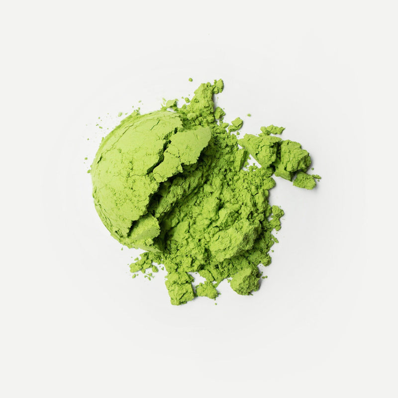 A mound of vibrant green organic matcha powder from Rishi Tea & Botanicals, stone-milled on Nishi-san’s farm, is scattered across a crisp white background.