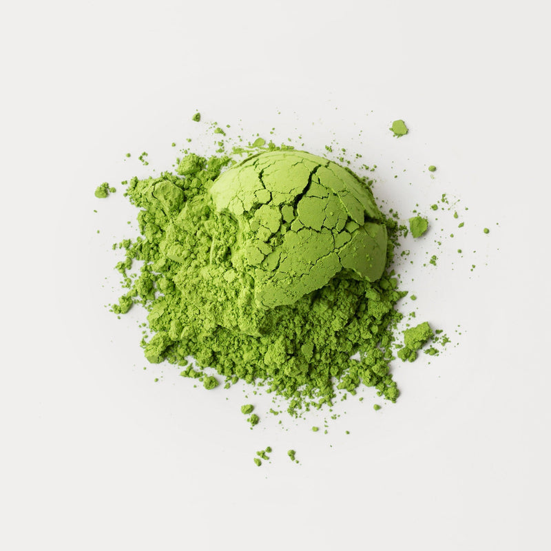 A vibrant heap of Rishi Tea & Botanicals organic matcha powder, rich in umami, is scattered on a white surface.