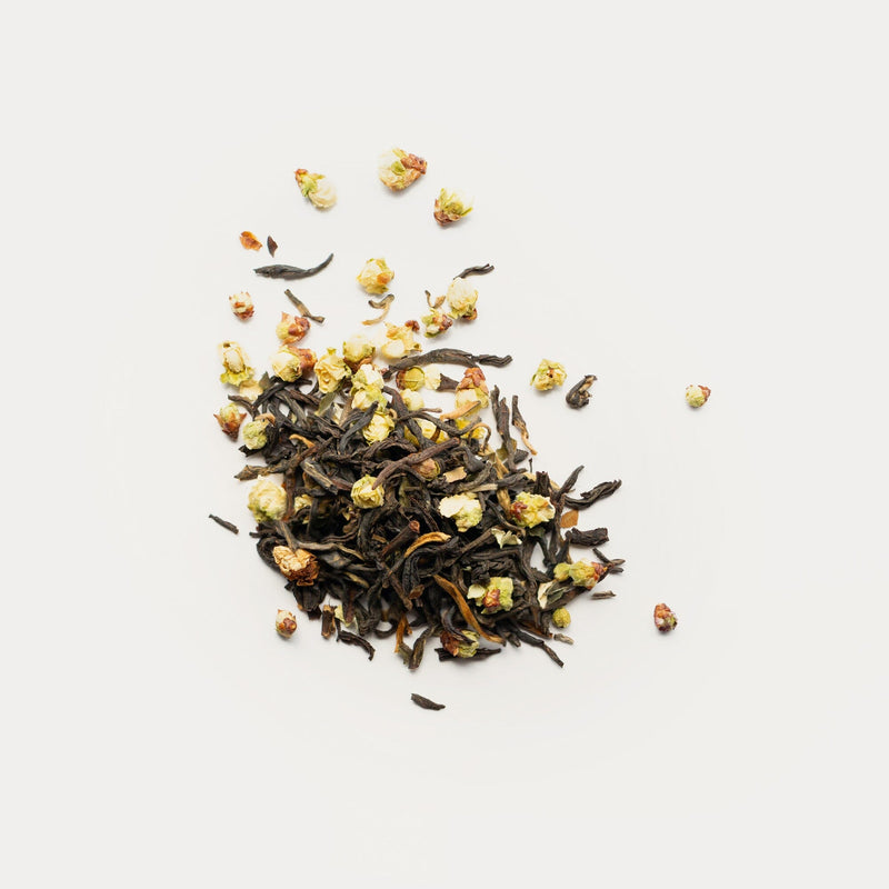 Rishi Tea & Botanicals’ loose leaf Dian Hong red tea blended with dried plum blossoms and scattered flowers creates a vibrant display on white, exuding a fruity-floral aroma.
