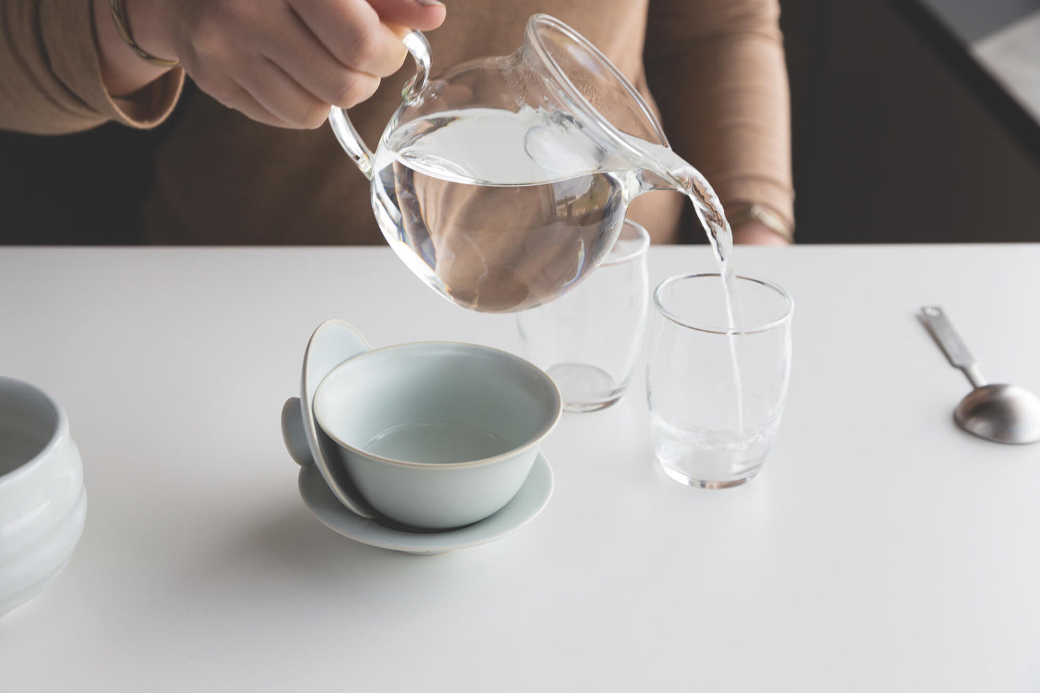 Close-up of clear teacups as part of the gaiwan set, showing how to use warm water as part of the preparation