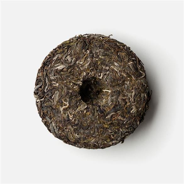A Laos Sheng Pu’er Tea Cake Vintage 2021 from Rishi Tea & Botanicals on a white surface.